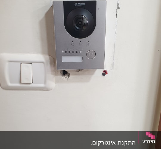 אינטרקום מותקן על קיר עם מצלמה וכפתור פעמון